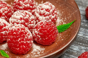A dessert of fresh ripe raspberries and powdered sugar closeup on wooden plate on a background of black and white cutting Board