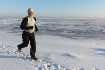 Fototapeta na wymiar Mature man in a beige sweater running across the ice of a frozen river , Ob Reservoir, Russia