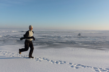 Mature man in a beige sweater running across the ice of a frozen river , Ob Reservoir, Russia