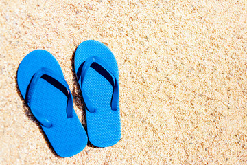 Fototapeta na wymiar Blue sandal flip-flops on yellow sand. Summer fun time and accessories on the beach, summer vacations, copy space.
