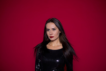 Close up Portrait of a beautiful woman with a beautiful make-up in a black dress on a red background. St. Valentine's Day or Women's Day. March 8. Fashion Concept