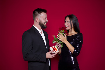 A man gives a present to his woman. Beautiful young couple in love on a red background. Valentine's Day. Women's Day. March 8
