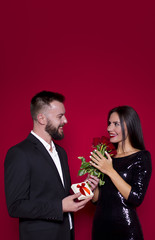 A man gives a present to his woman. Beautiful young couple in love on a red background. Valentine's Day. Women's Day. March 8