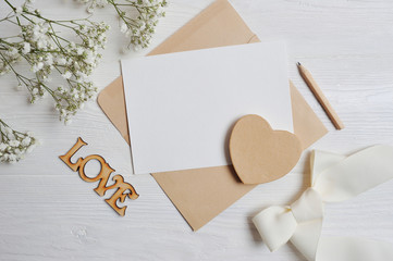 Mock up letter with a love box in the shape of a heart lies on a wooden white table with gypsophila flowers, a greeting card for Valentine's Day with a place for your text. Flat lay, top view photo