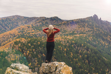 Obraz premium A girl in a red jacket looks out into the distance on a mountain, a view of the mountains and an autumnal forest by an overcast day. Free space for text