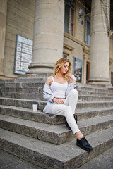 Fototapeta na wymiar Stylish curly blonde model girl wear on white with cup of coffee posing on stairs outdoor.