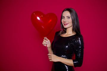 Holiday for women. Beautiful woman in a black dress with a ball in her hands on a red background. St. Valentine's Day or Women's Day.