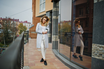 Fototapeta premium Stylish curly blonde model girl wear on white with cup of coffee at hand posing against large window.