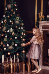Sisters in front of the fir-tree and fireplace with candles and gifts. New year's eve. Christmas eve. Cozy holiday at the fir-tree with lights and gold decor.