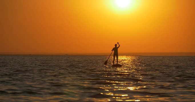 SUP at sunset. Woman paddlingg towords the sunset