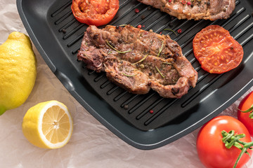Grilled steak on grill pan with tomatoes and lemon on white background