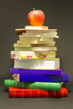 Concept of education. Stack of school books with a red apple on top in front of dark gray background