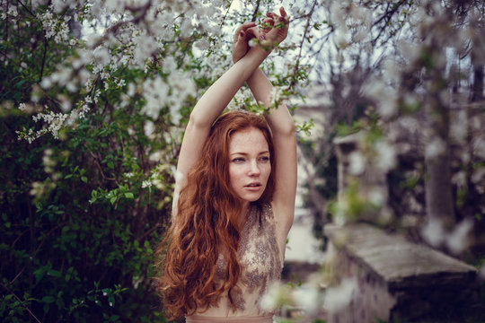 Beautiful happy young woman with red hair enjoying smell in a flowering spring garden