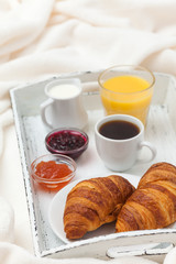 Freshly baked croissant, orange juice, jam, cup of black coffee on white wooden tray on plaid. Homemade cookie. Fresh pastries for breakfast. Delicious dessert. Closeup photography. Vertical banner