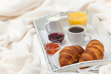 Freshly baked croissant, orange juice, jam, cup of black coffee on white wooden tray on plaid. Homemade cookie. Fresh pastries for breakfast. Delicious dessert. Closeup photography. Horizontal banner