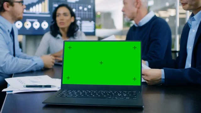 In the Meeting Room Laptop with Green Chroma Key Screen on the Conference Table. In the Background Business People Have Important Discussion. Shot on RED EPIC-W 8K Helium Cinema Camera.