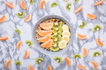 Healthy Breakfast set Granola with tangerines. Rolled Oat flakes in bowl with orange, kiwi and banana slices. Marble background.