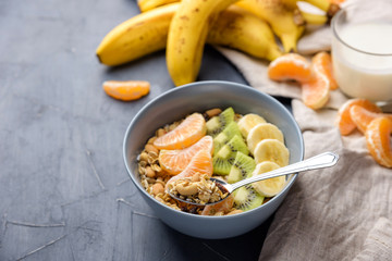 Healthy Breakfast set Granola with tangerines. Rolled Oat flakes in bowl with orange, kiwi and banana slices. Grey background, napkin. Cup of yoghurt