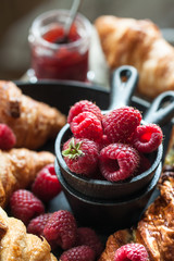 Gourmet croissant and danish buns with fresh raspberry and jam for the breakfast on the cast iron tray and wooden table