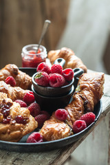 Gourmet croissant and danish buns with fresh raspberry and jam for the breakfast on the cast iron tray and wooden table