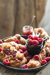 Gourmet croissant and danish buns with fresh raspberry and jam for the breakfast on the cast iron tray and wooden table