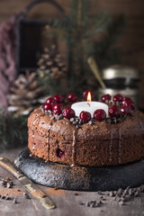 Double chocolate cherry cake with spices and big candle on the rustic background for winter holidays. Christmas and New Year decoration