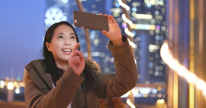 Asian woman taking photo on cellphone in the city of Hong Kong at night, bokeh city background