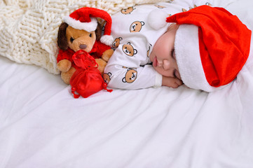 Little baby boy sleeping in pajamas and Santa hat with a toy dog and a gift in a red bag