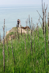 Look from the green grass at wedding couple standing on the cliff