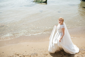 Fototapeta na wymiar Blonde bride whirls on the sea shore