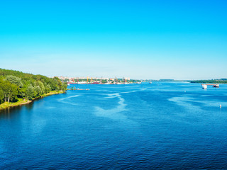 Wide River With Sailing Boats And Green Woody Riverbank In City