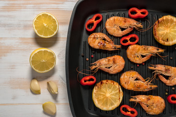 Grilled shrimps on a grill frying pan with lemon, paprika, spices and herbs. Wooden background.