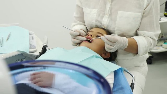 Dentist hands take from table a dental proba and examining a teeth of little girl. Dentist using a mirror and dental proba. Camera movement.