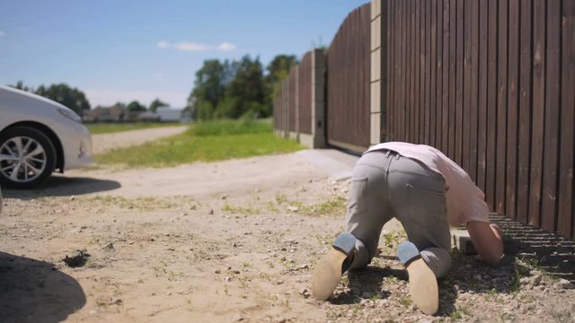 A man on the knees trying to open a driveway wooden gates while the neighbor opens her automatic gates