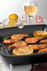 Grilled shrimps on a grill frying pan with wine, lemon, paprika, spices and herbs. Wooden background.