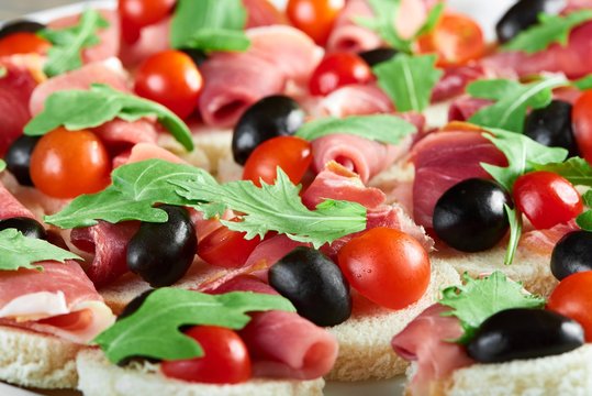 Delicious restaurant appetizer : canapees with white bread,bacon rolls,fresh cherry tomatoes and green parsley leaves. Tasty snack for catering or buffet.