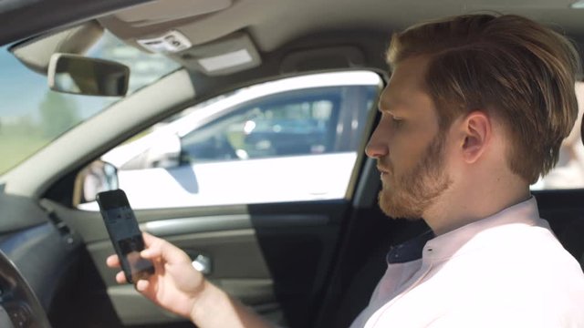 Man in a car with the smartphone flirts and smiles with a woman in a nearby car