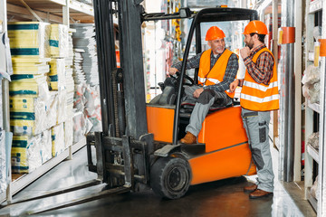 two male workers using forklift machine in storehouse