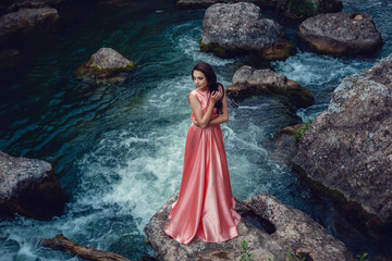 River witch, sitting on a rock in river. Pink long dress, a fabulous image.Fashionable toning....