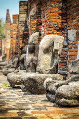Fototapeta premium Headless Buddha statues along a temple wall at Wat Mahathat, Temple of the Great Relic, in Ayutthaya, Thailand
