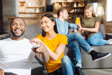 Funny comedy.  Joyful sweet young  couple sitting next to each other while she placing hands on his shoulder and staring at him