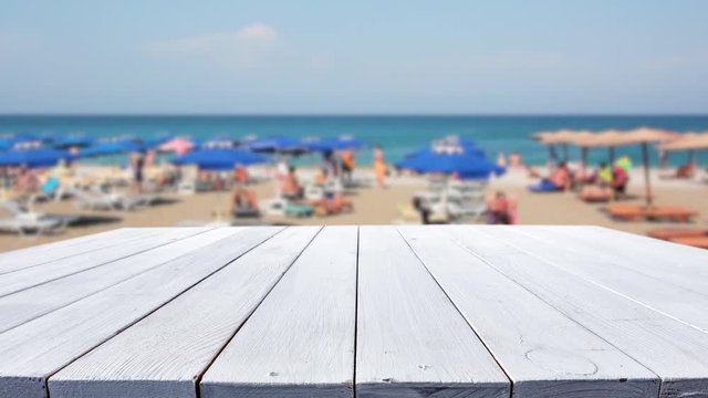 White desk of free space for your product, packshot, or motion. Blurred background of sea and beach with few people. 