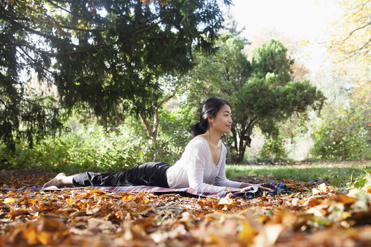 Smiling woman performing yoga while lying on picnic blanket at park during autumn