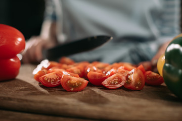 cropped image of cook cutting cherry tomatoes on wooden board