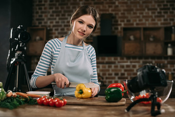 young food blogger cutting bulgarian peppers and looking at camera