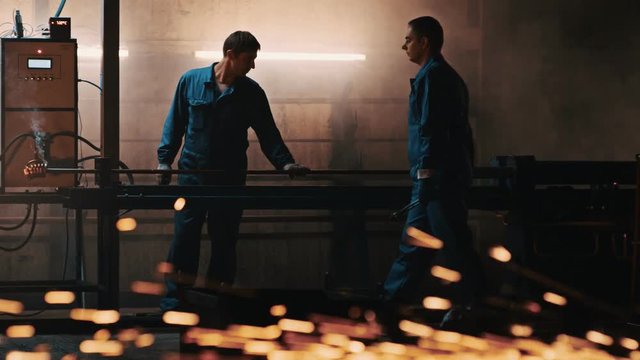 Industrial employees using inversion heater for metal piece in production hall