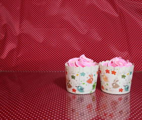 Two cup cake on the red fabric and white dot pattern with colorful rounded sugar beads and reflect floor. cupcake is a small cake baked in a cup-shaped container.