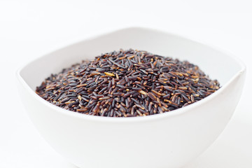 Thai Black or dark brown raw rice in a white bowl for a healthy diet. High fiber, vitamin, carbohydrate, minerals, and nutrition for healthy people. on the white background, isolate.
