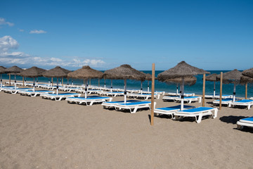 Fototapeta na wymiar Line of straw beach umbrellas and sun loungers with clear blue sea and sky in background