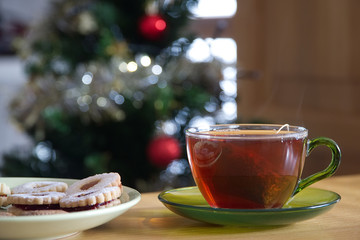 A cup of black tea a plate of cookies with a blurred Christmas tree at the background                            
